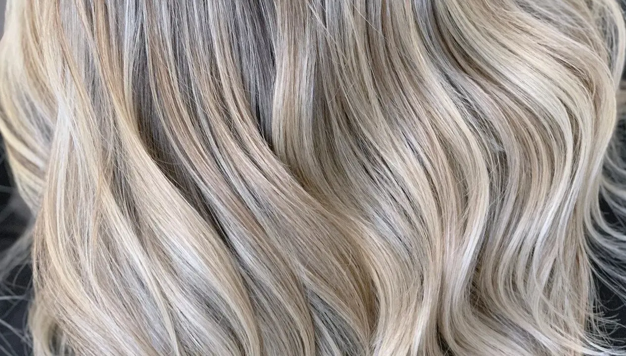 Falujące pasma włosów w odcieniu zimny beżowy blond, z subtelnymi refleksami tworzącymi efekt głębi.