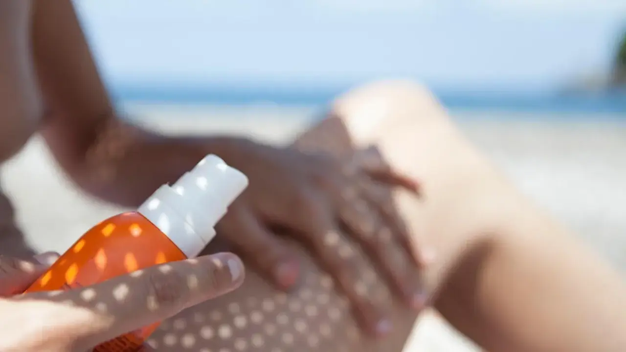 Ochrona przed słońcem na plaży. Ręka aplikuje spray z filtrem UV na nogę, zapewniając skuteczną fotoprotekcję.