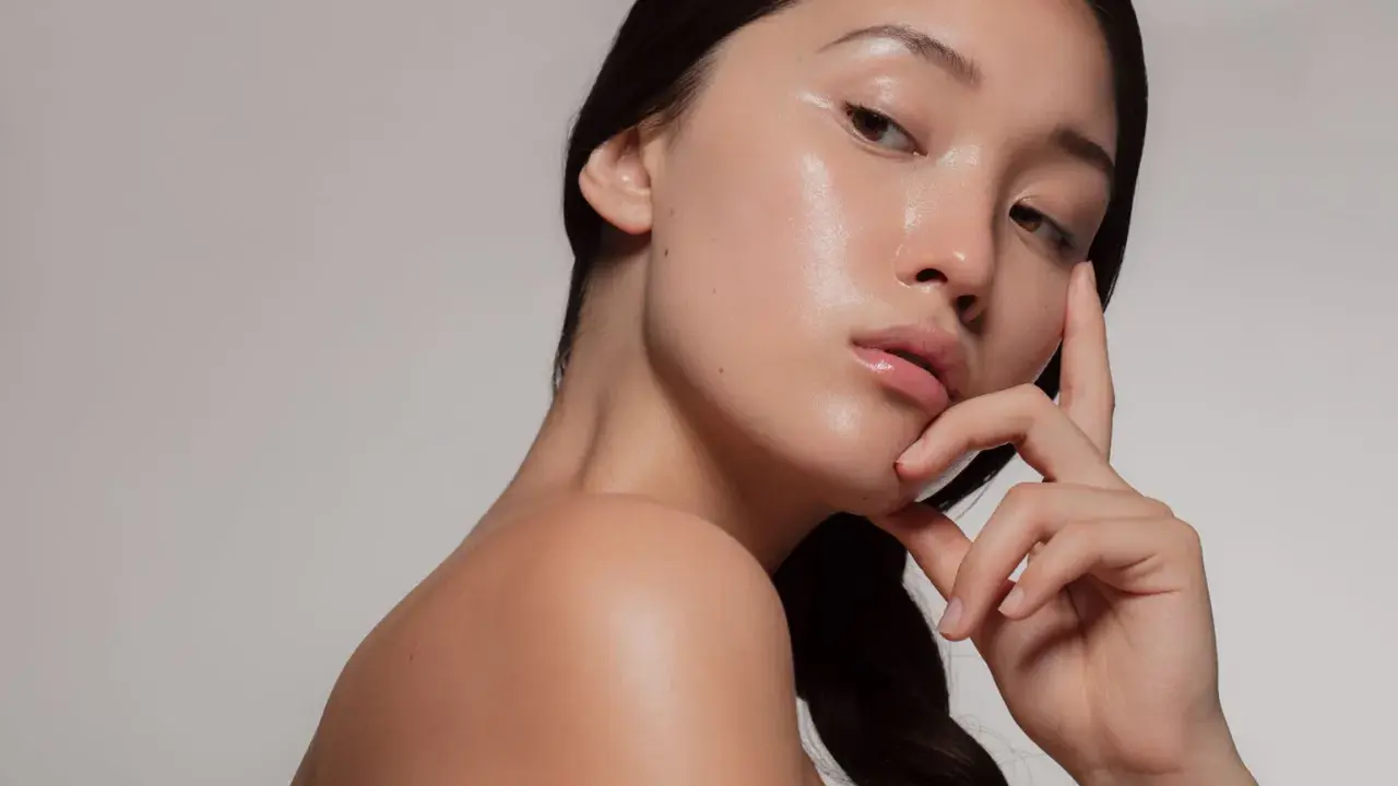 Młoda kobieta z idealną, lśniącą cerą typu "glass skin", delikatnie dotykająca twarzy.