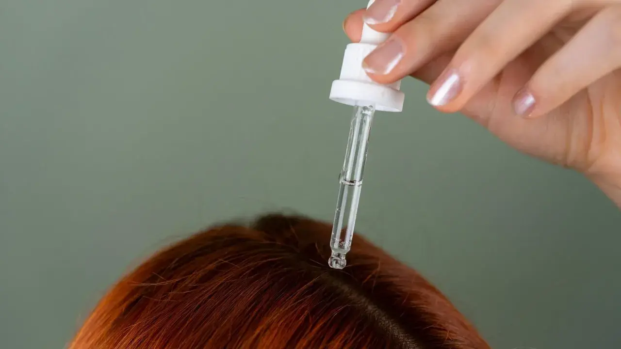 Dłoń z pipetką aplikuje serum na rudą skórę głowy, pokazując, jak nawilżyć skórę głowy.