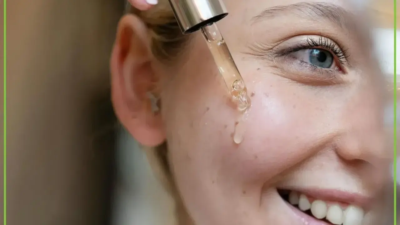 Kropla serum z pipety spada na policzek uśmiechniętej kobiety. Dowiedz się, jak stosować retinol dla pięknej cery.