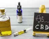 Butelka z olejkiem, strzykawka i tabliczka z napisem CBD. Zastanawiasz się, olejek CBD na co?