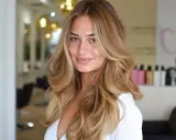Uśmiechnięta blondynka z fryzurą butterfly cut, z falowanymi włosami i refleksami.