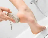Dłoń trzyma pumeks, którym delikatnie ściera się naskórek z pięty.