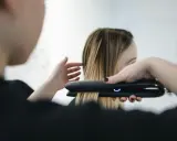 Stylist prostuje włosy po trwałej prostownicą.