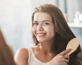 Uśmiechnięta kobieta szczotkuje swoje długie, lśniące włosy, ciesząc się efektem bond repair.