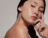 Młoda kobieta z idealną, lśniącą cerą typu "glass skin", delikatnie dotykająca twarzy.