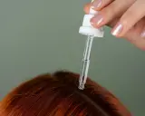 Dłoń z pipetką aplikuje serum na rudą skórę głowy, pokazując, jak nawilżyć skórę głowy.