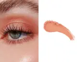 Delikatny makijaż oka w odcieniach brzoskwini, z subtelnym połyskiem. Obok próbka pudrowego różu, niczym delikatny **peach fuzz**.
