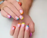Dłonie z paznokciami w stylu french manicure, gdzie końcówki zdobi tęczowy french kolor.