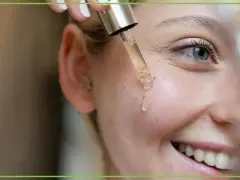 Kropla serum z pipety spada na policzek uśmiechniętej kobiety. Dowiedz się, jak stosować retinol dla pięknej cery.
