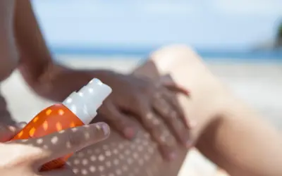 Ochrona przed słońcem na plaży. Ręka aplikuje spray z filtrem UV na nogę, zapewniając skuteczną fotoprotekcję.