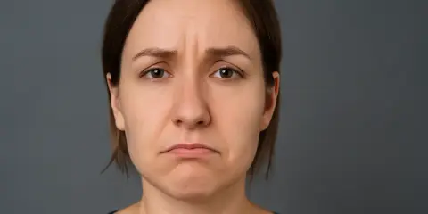 Smutna twarz z opadającymi kącikami ust i zmarszczonymi brwiami.
