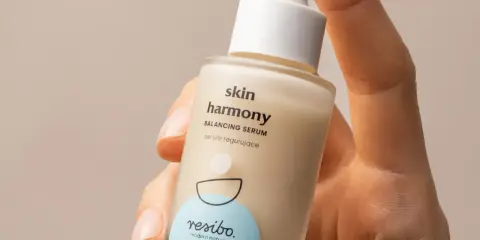 Dłoń trzyma buteleczkę serum Resibo z alantoiną. Skóra harmonijnie odzyskuje równowagę dzięki temu produktowi.