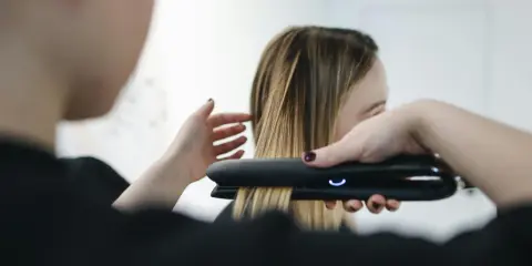 Stylist prostuje włosy po trwałej prostownicą.