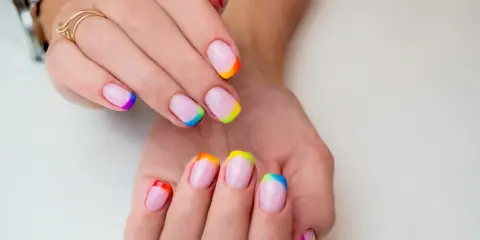 Dłonie z paznokciami w stylu french manicure, gdzie końcówki zdobi tęczowy french kolor.