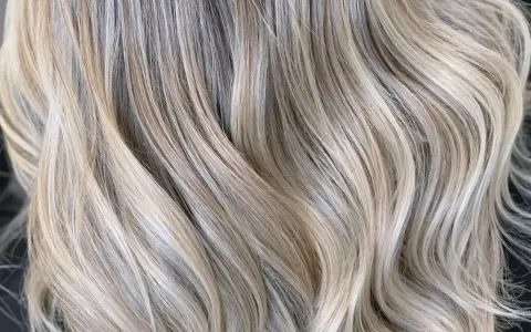 Falujące pasma włosów w odcieniu zimny beżowy blond, z subtelnymi refleksami tworzącymi efekt głębi.