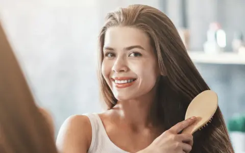Uśmiechnięta kobieta szczotkuje swoje długie, lśniące włosy, ciesząc się efektem bond repair.