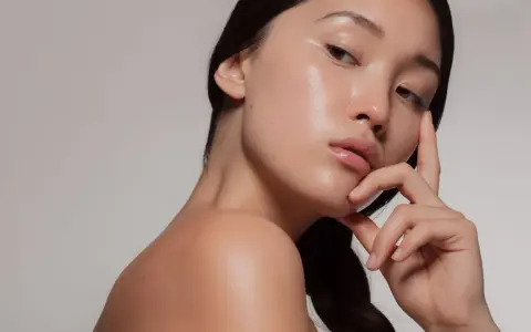 Młoda kobieta z idealną, lśniącą cerą typu "glass skin", delikatnie dotykająca twarzy.