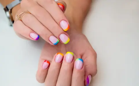Dłonie z paznokciami w stylu french manicure, gdzie końcówki zdobi tęczowy french kolor.