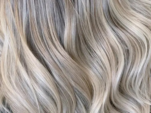 Falujące pasma włosów w odcieniu zimny beżowy blond, z subtelnymi refleksami tworzącymi efekt głębi.