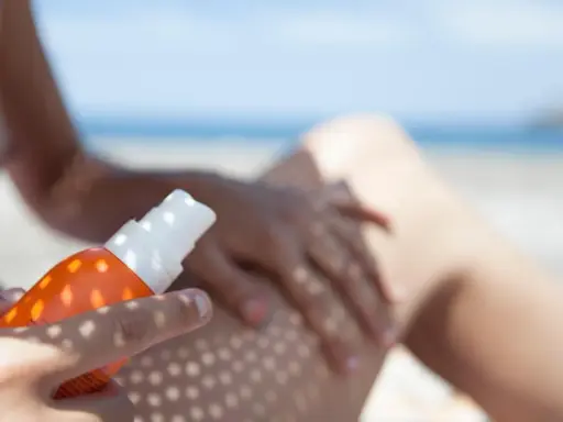 Ochrona przed słońcem na plaży. Ręka aplikuje spray z filtrem UV na nogę, zapewniając skuteczną fotoprotekcję.