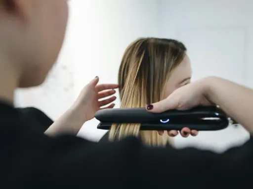 Stylist prostuje włosy po trwałej prostownicą.
