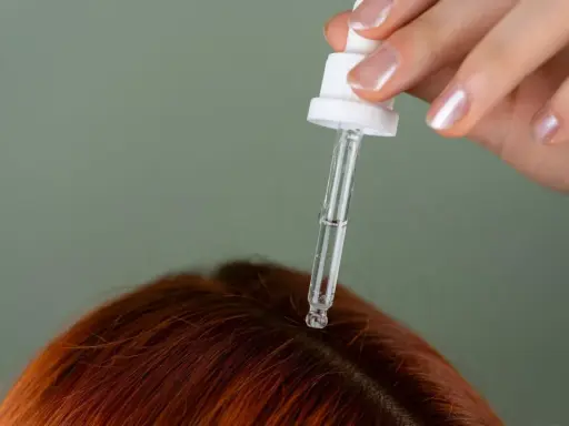 Dłoń z pipetką aplikuje serum na rudą skórę głowy, pokazując, jak nawilżyć skórę głowy.