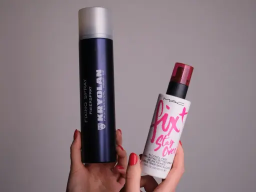 Dwie ręce trzymają dwa spraye: duży, granatowy Kryolan Fixing Spray i mniejszy, biały Fix+ Stay Over MAC. Oba to profesjonalne produkty typu fixer.