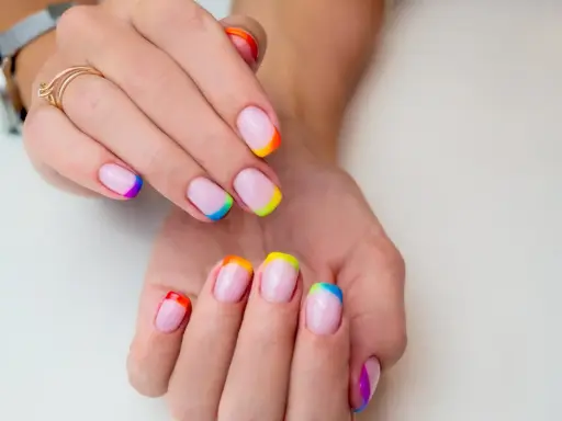 Dłonie z paznokciami w stylu french manicure, gdzie końcówki zdobi tęczowy french kolor.