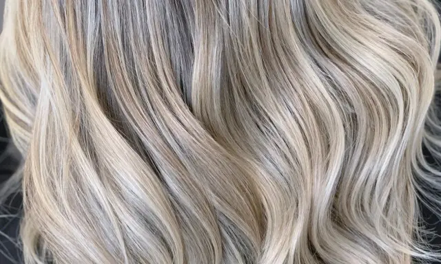 Falujące pasma włosów w odcieniu zimny beżowy blond, z subtelnymi refleksami tworzącymi efekt głębi.