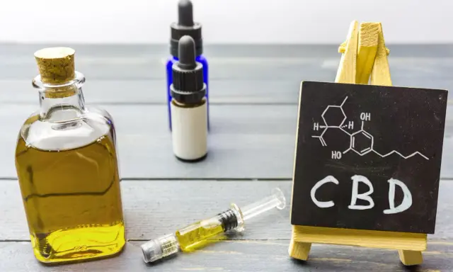 Butelka z olejkiem, strzykawka i tabliczka z napisem CBD. Zastanawiasz się, olejek CBD na co?