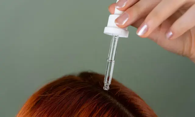Dłoń z pipetką aplikuje serum na rudą skórę głowy, pokazując, jak nawilżyć skórę głowy.