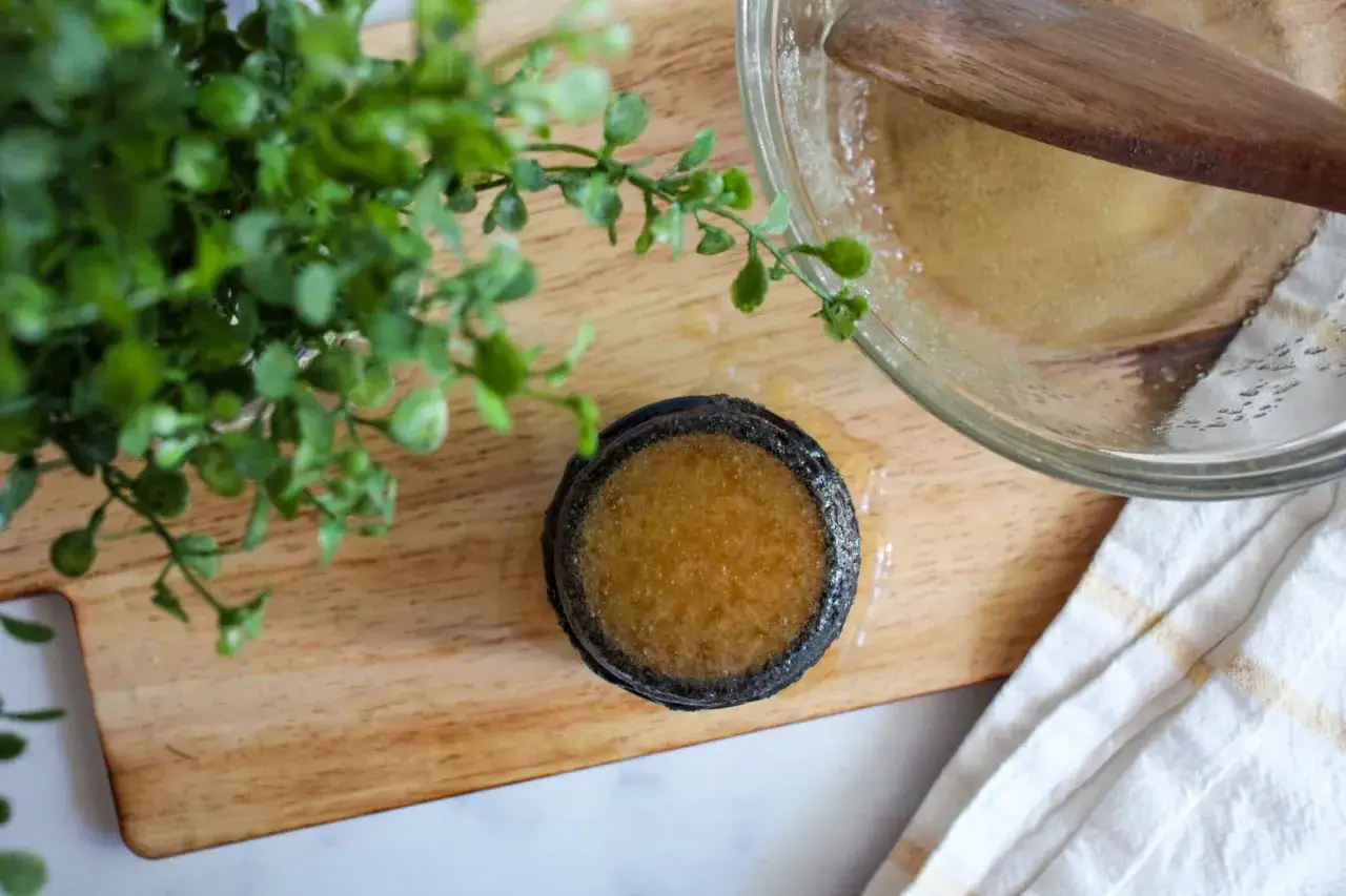 Gotowy domowy peeling do skóry głowy w słoiczku, obok miseczki z mieszanką i drewnianej łyżki.