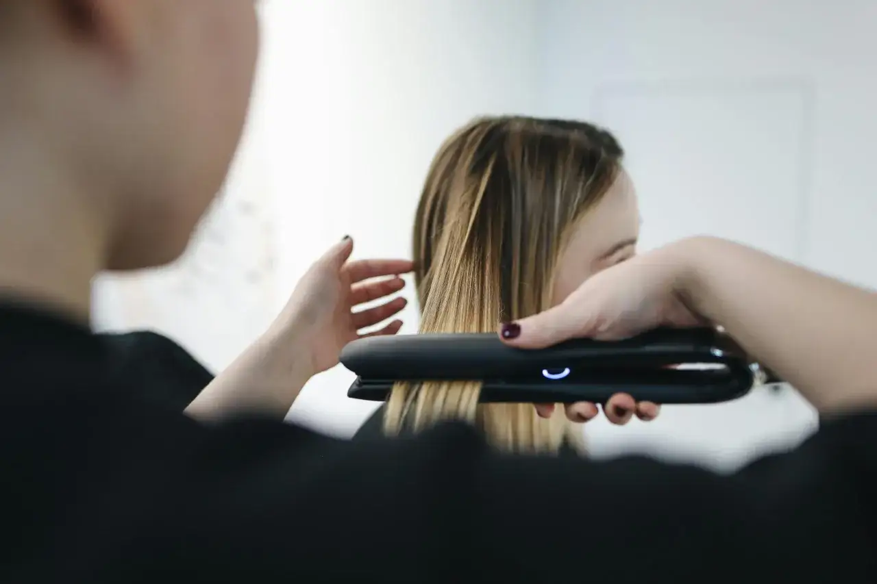 Stylist prostuje włosy po trwałej prostownicą.