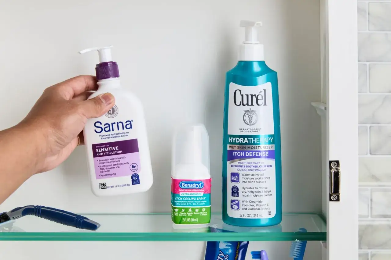 Ręka trzyma Sarna Sensitive Anti-Itch Lotion, obok spray Benadryl i Curél Hydratherapy. Produkty te to skuteczny maść na alergie skórną.