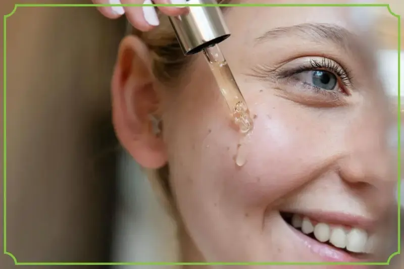 Kropla serum z pipety spada na policzek uśmiechniętej kobiety. Dowiedz się, jak stosować retinol dla pięknej cery.